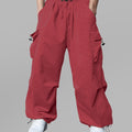 Man in red baggy sweatpants, high waist, five pockets, back logo. White sneakers, standing front.