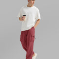 Side view of man in red baggy sweatpants holding coffee cup, showing side pocket details.