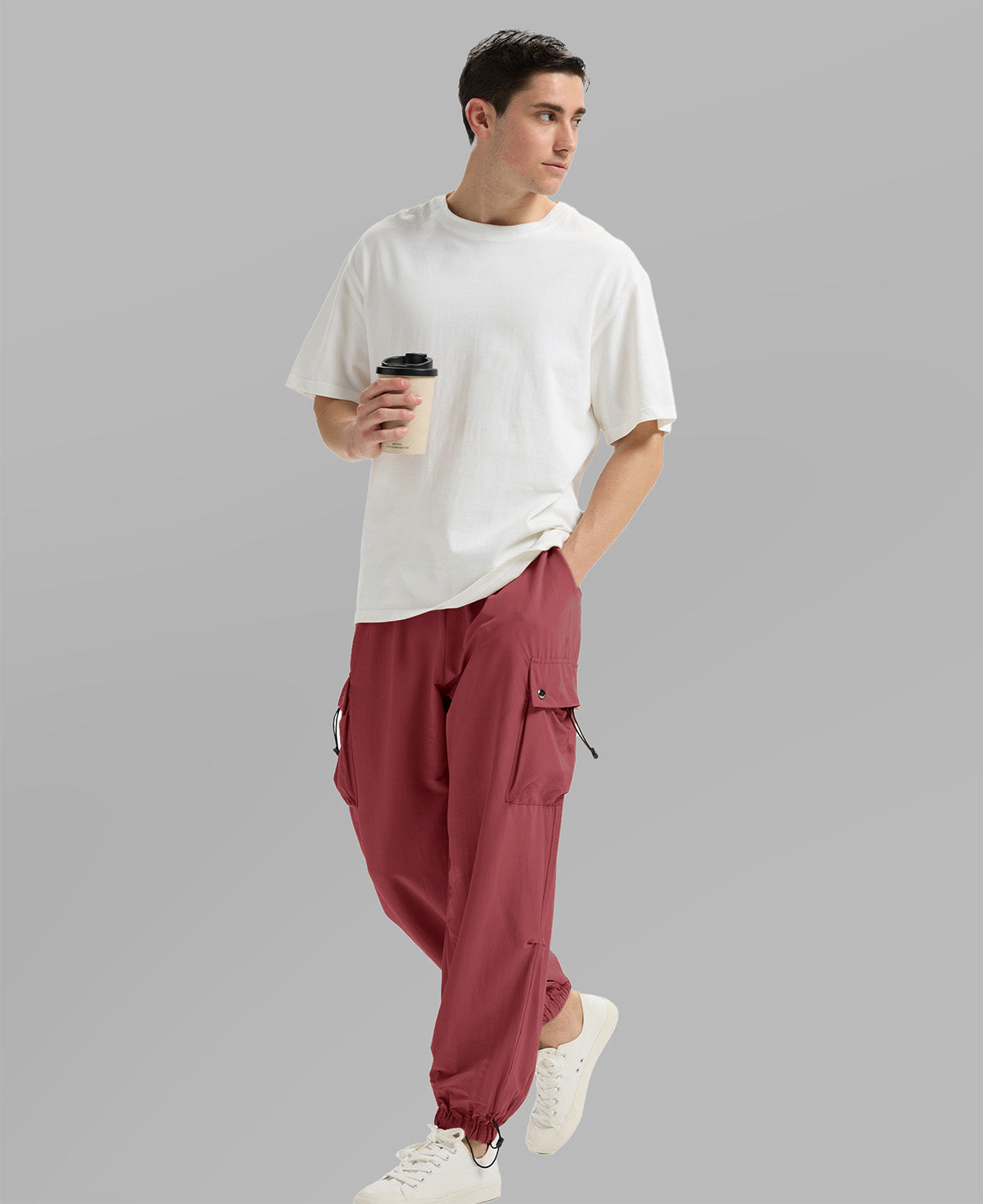 Side view of man in red baggy sweatpants holding coffee cup, showing side pocket details.