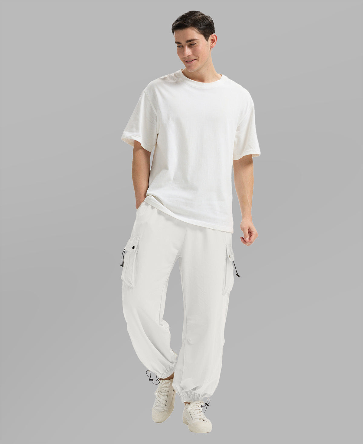 Full view of man wearing white baggy sweatpants with white tee and sneakers, highlighting fit.