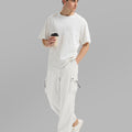 Side view of man in white baggy sweatpants holding coffee cup, showing side pocket details.