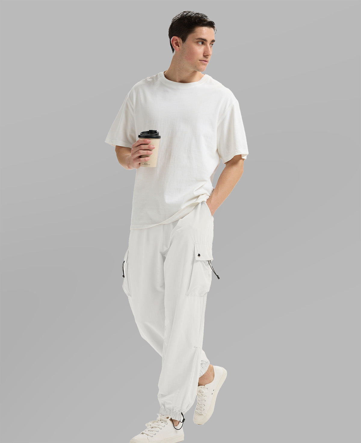 Side view of man in white baggy sweatpants holding coffee cup, showing side pocket details.