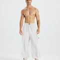 Bare-chested man in white baggy sweatpants, white shoes, highlighting waist and length details.