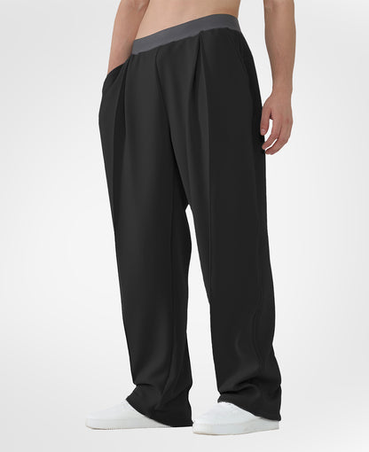 Man in black pleated baggy sweatpants with white shoes, hand in pocket, showcasing wide leg and contrasting elastic waist.