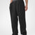 Man in black pleated baggy sweatpants with white shoes, hand in pocket, showcasing wide leg and contrasting elastic waist.