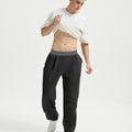 Man wearing white tee and black men's pleated baggy sweatpants, lifting shirt to show waist detail and fit.
