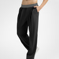Side view of black wide-leg sweatpants showing front pleats and drape, hand in pocket highlighting pocket design.