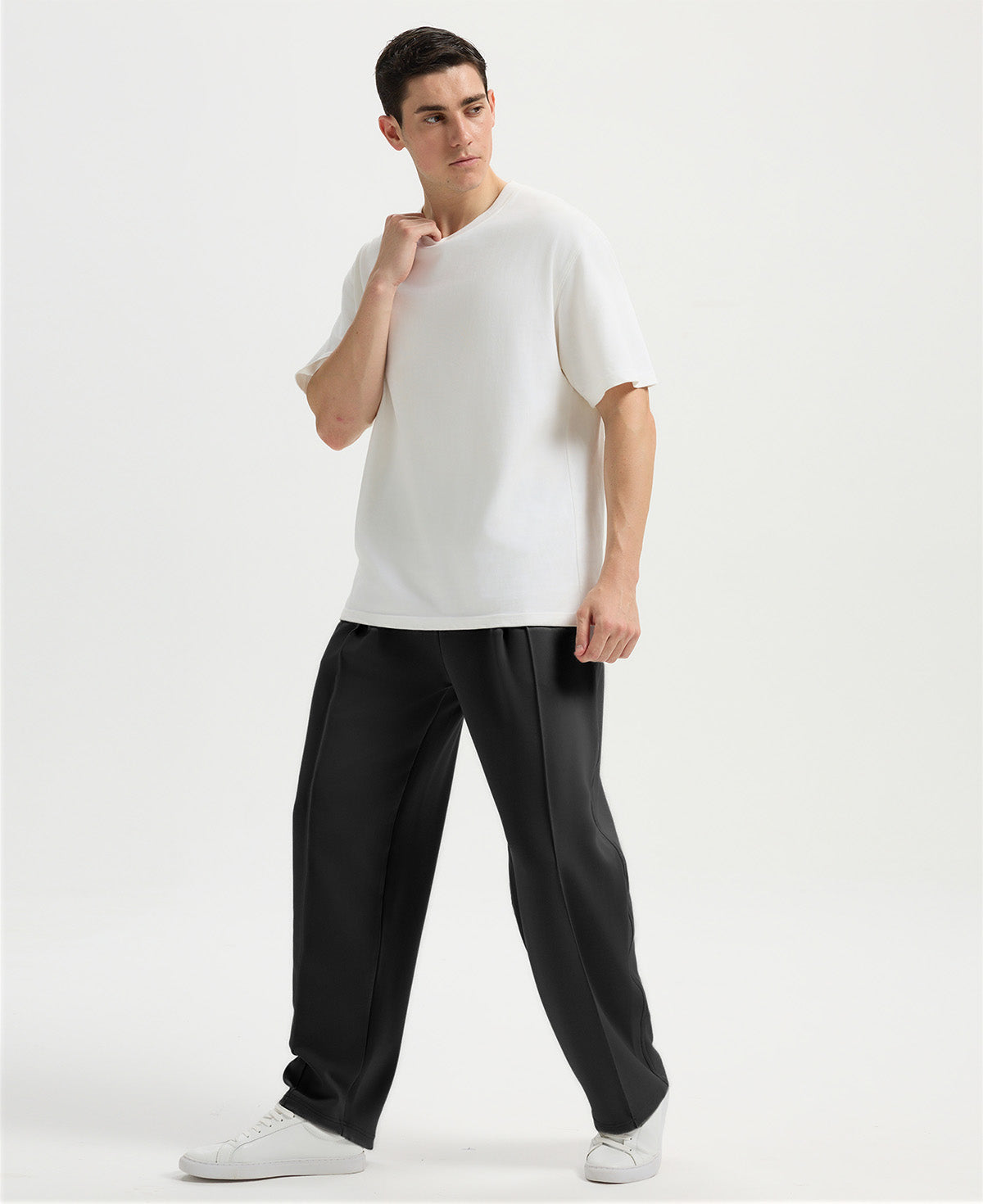 Man in white tee and black wide-leg sweatpants standing naturally, showcasing simple everyday style.