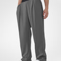 Man in dark grey pleated baggy sweatpants with white shoes, hand in pocket, showcasing wide leg and contrasting elastic waist.