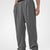 Man in dark grey pleated baggy sweatpants with white shoes, hand in pocket, showcasing wide leg and contrasting elastic waist.
