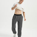 Man wearing white tee and dark grey men's pleated baggy sweatpants, lifting shirt to show waist detail and fit.