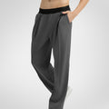 Side view of dark grey wide-leg sweatpants showing front pleats and drape, hand in pocket highlighting pocket design.