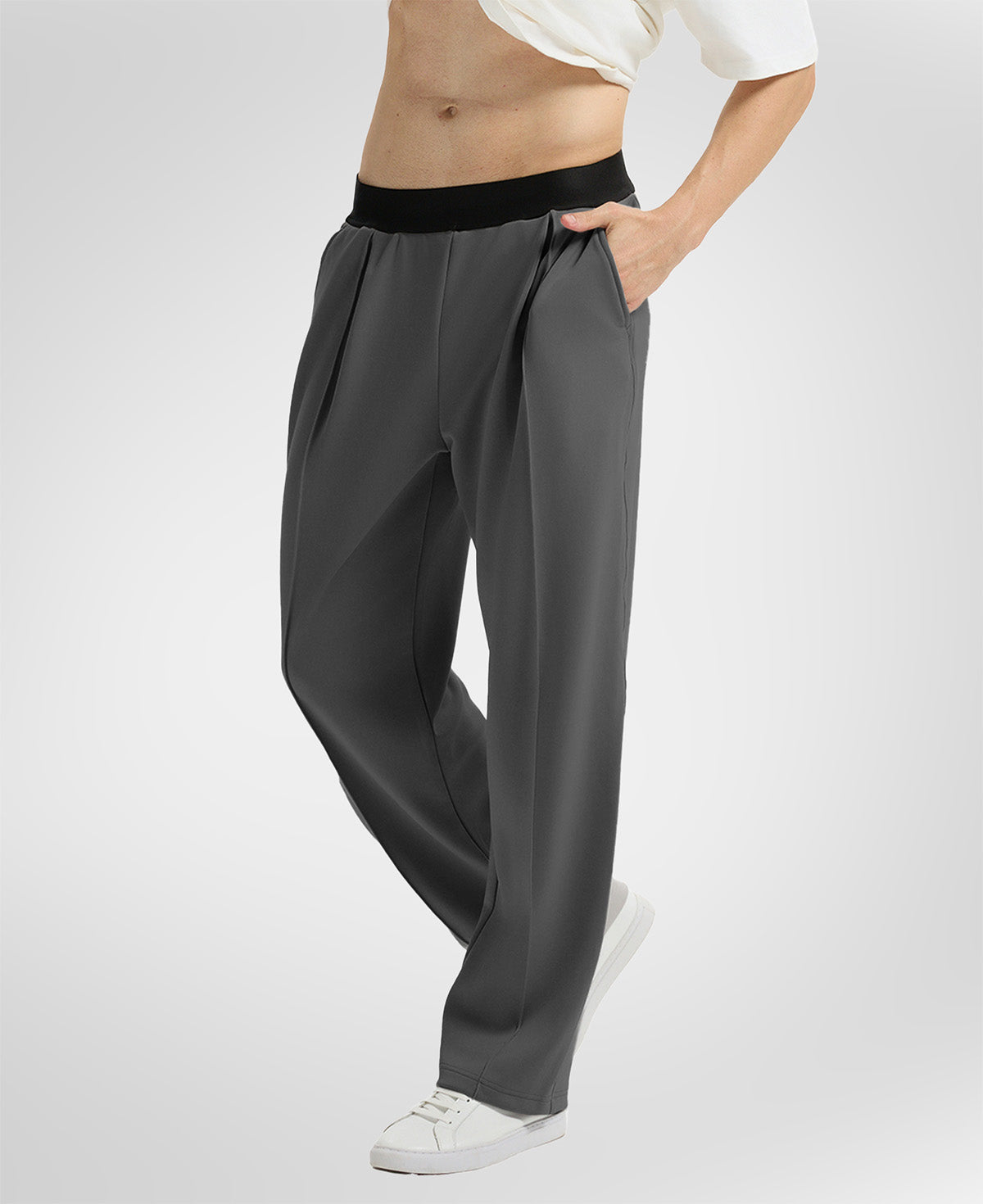 Side view of dark grey wide-leg sweatpants showing front pleats and drape, hand in pocket highlighting pocket design.
