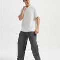 Man in white tee and dark grey wide-leg sweatpants standing naturally, showcasing simple everyday style.