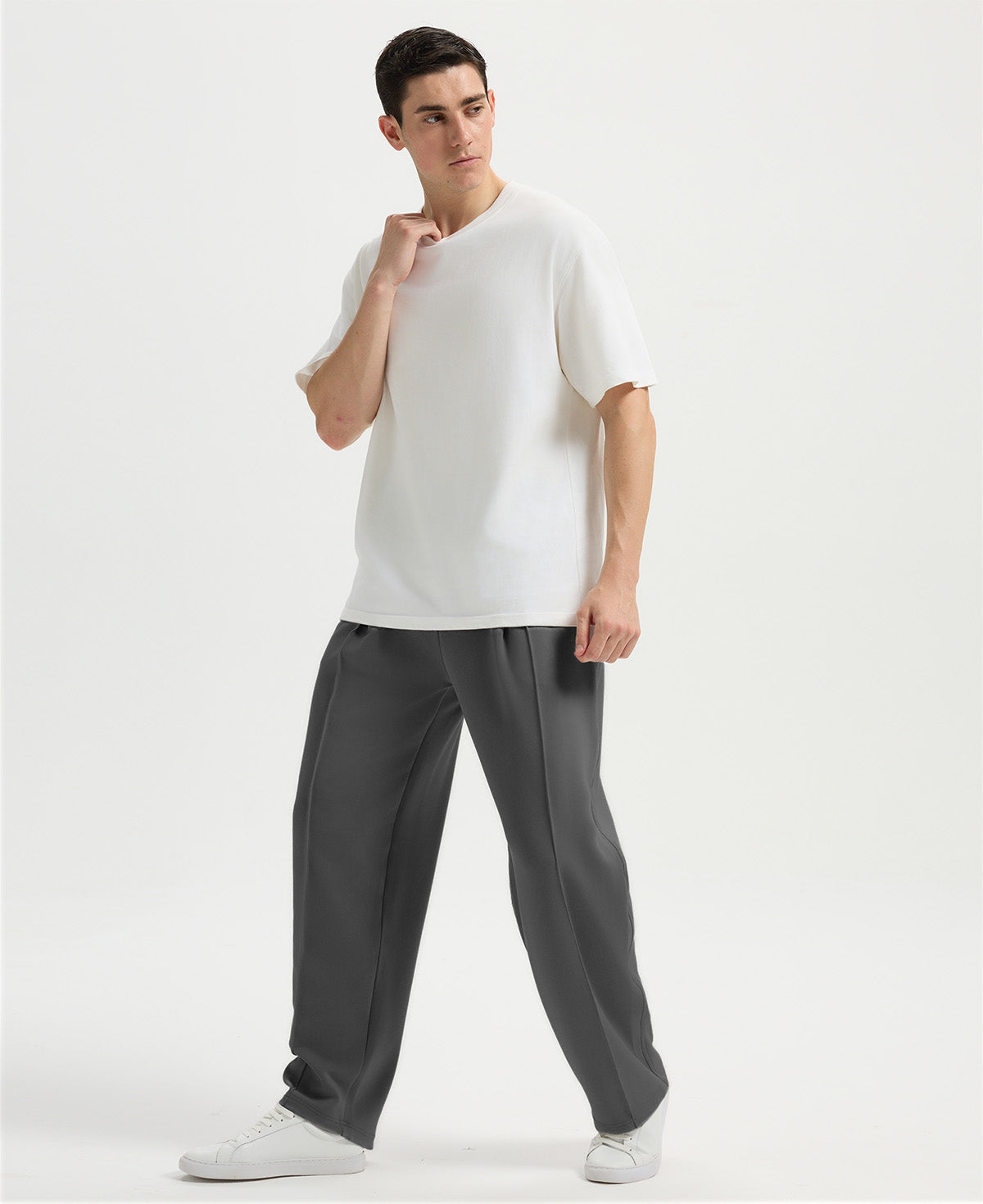 Man in white tee and dark grey wide-leg sweatpants standing naturally, showcasing simple everyday style.