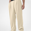 Man in khaki pleated baggy sweatpants with white shoes, hand in pocket, showcasing wide leg and contrasting elastic waist.