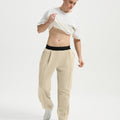 Man wearing white tee and khaki men's pleated baggy sweatpants, lifting shirt to show waist detail and fit.