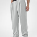 Man in light grey pleated baggy sweatpants with white shoes, hand in pocket, showcasing wide leg and contrasting elastic waist.