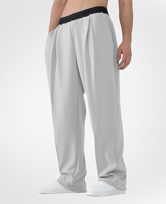 Man in light grey pleated baggy sweatpants with white shoes, hand in pocket, showcasing wide leg and contrasting elastic waist.