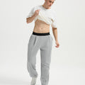 Man wearing white tee and light grey men's pleated baggy sweatpants, lifting shirt to show waist detail and fit.