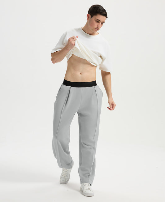 Man wearing white tee and light grey men's pleated baggy sweatpants, lifting shirt to show waist detail and fit.
