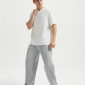 Man in white tee and light grey wide-leg sweatpants standing naturally, showcasing simple everyday style.