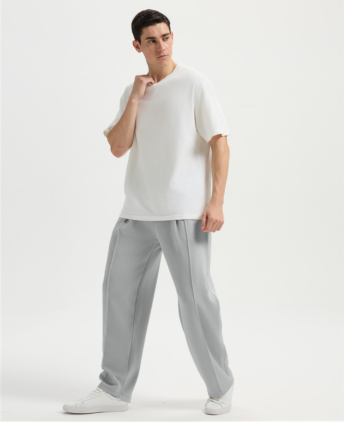 Man in white tee and light grey wide-leg sweatpants standing naturally, showcasing simple everyday style.