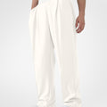 Man in white pleated baggy sweatpants with white shoes, hand in pocket, showcasing wide leg and contrasting elastic waist.