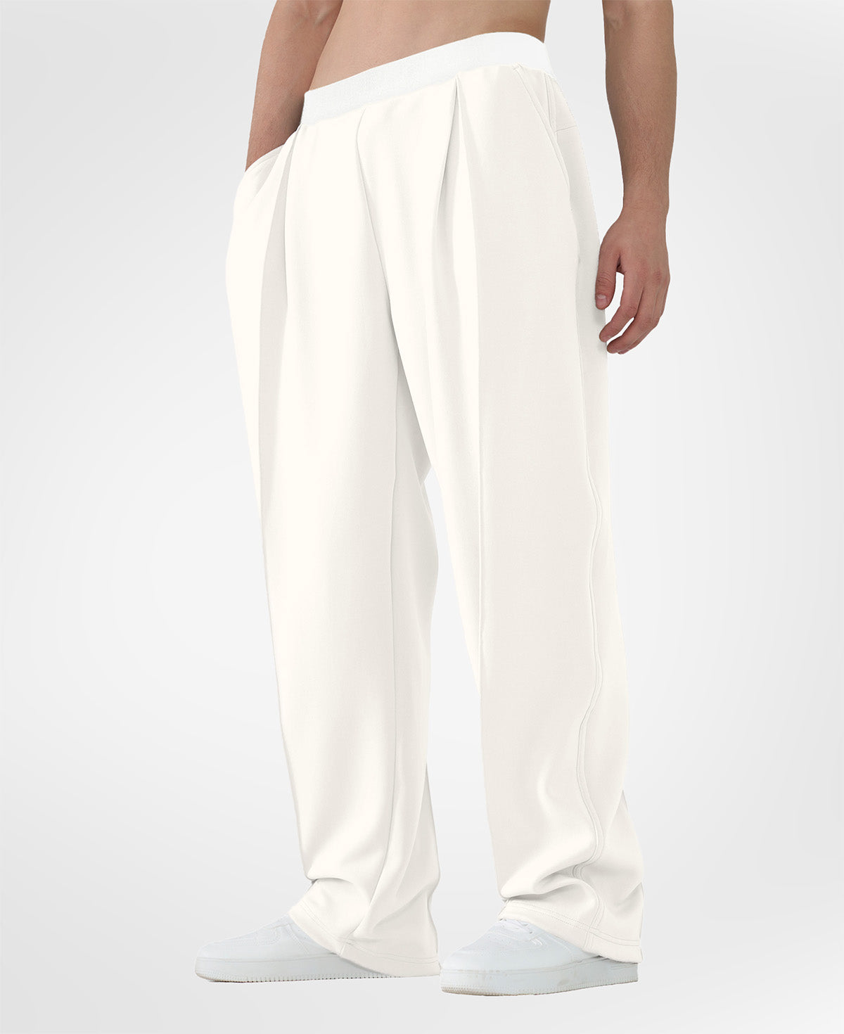Man in white pleated baggy sweatpants with white shoes, hand in pocket, showcasing wide leg and contrasting elastic waist.