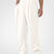 Man in white pleated baggy sweatpants with white shoes, hand in pocket, showcasing wide leg and contrasting elastic waist.