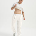 Man wearing white tee and white men's pleated baggy sweatpants, lifting shirt to show waist detail and fit.