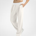Side view of white wide-leg sweatpants showing front pleats and drape, hand in pocket highlighting pocket design.