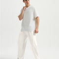 Man in white tee and white wide-leg sweatpants standing naturally, showcasing simple everyday style.