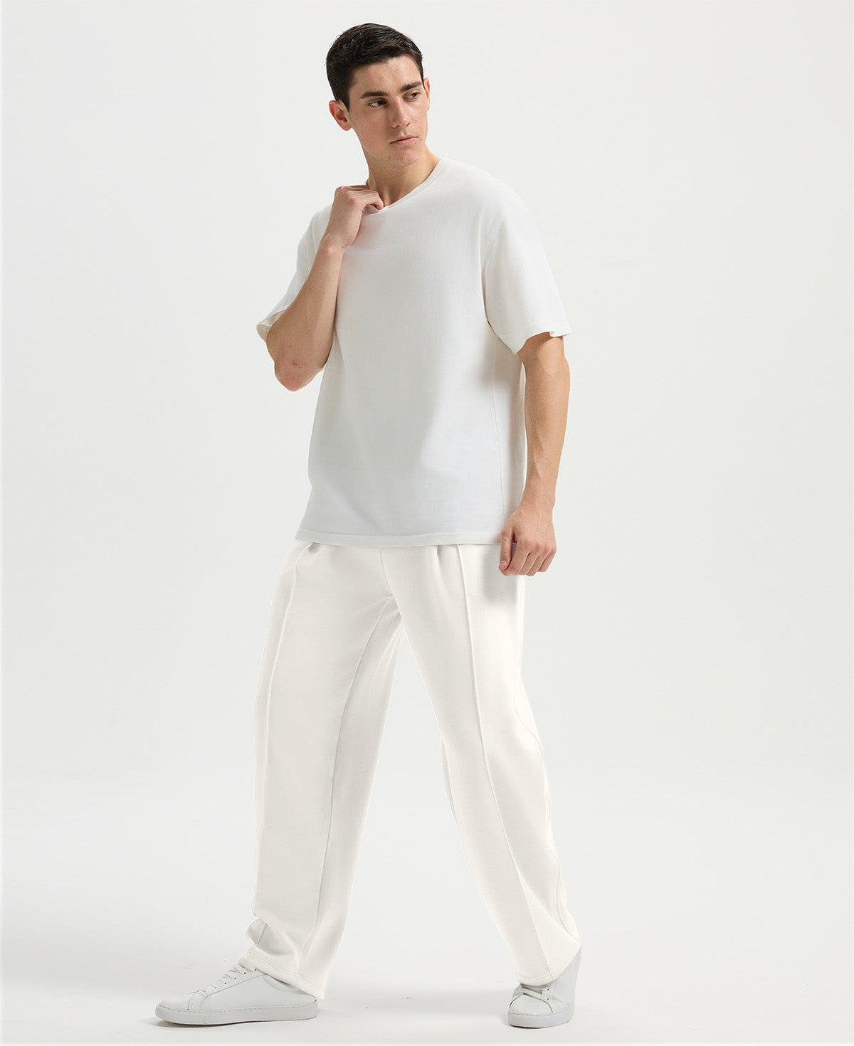 Man in white tee and white wide-leg sweatpants standing naturally, showcasing simple everyday style.