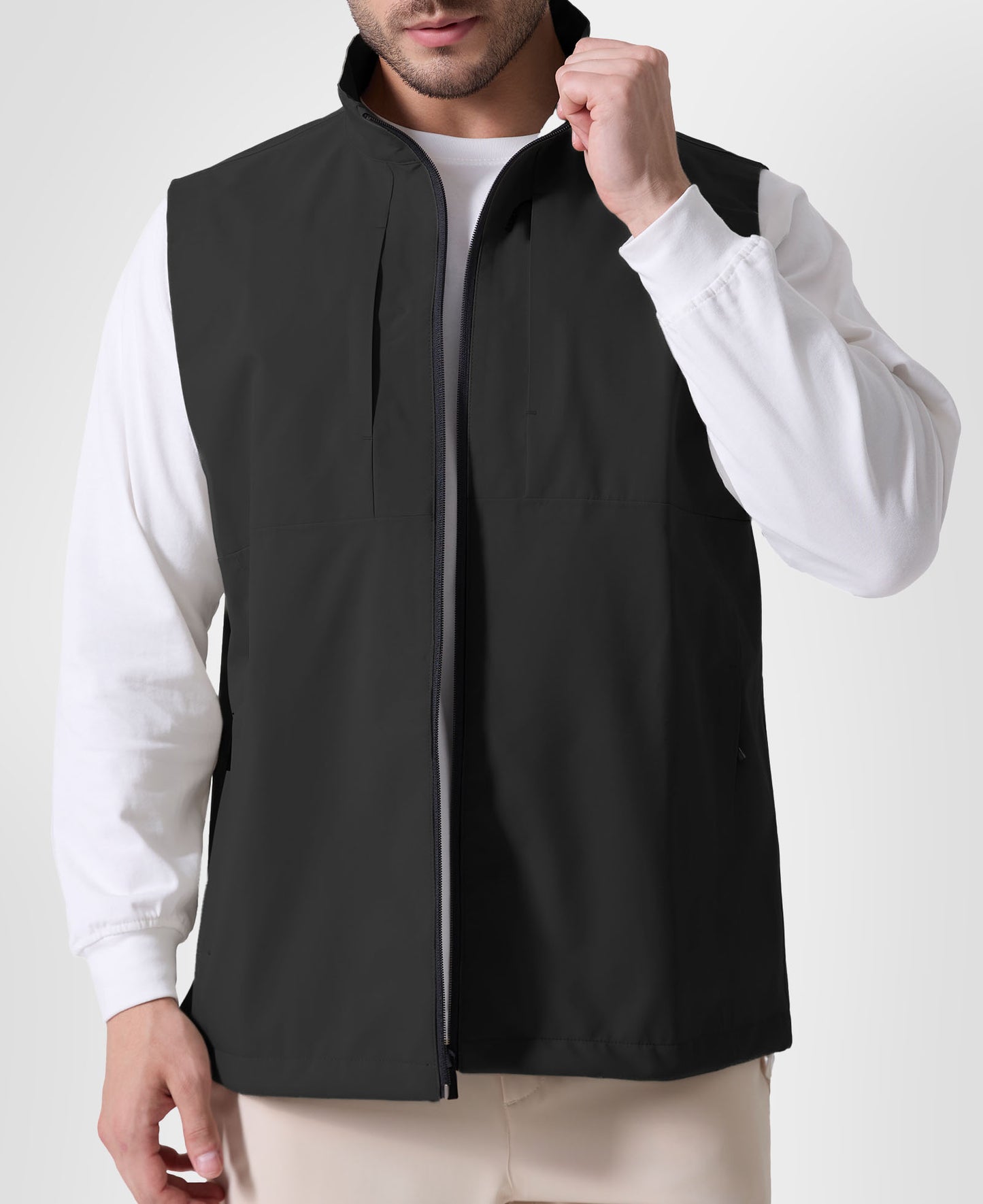 Man in black Men's Softshell Vest ¨C Lightweight Windproof Sleeveless, white long-sleeve tee & khaki pants, casual layered look.