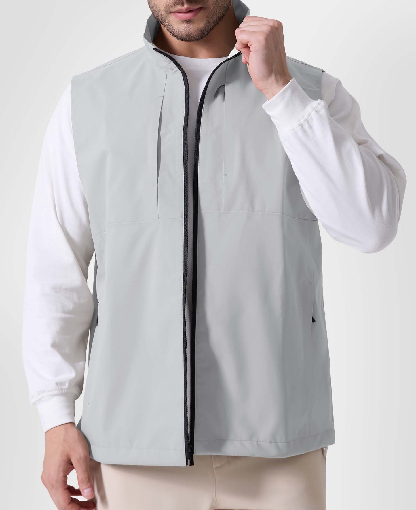 Man in white grey Men's Softshell Vest ¨C Lightweight Windproof Sleeveless, white long-sleeve tee & khaki pants, casual layered look.