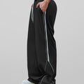 Man in black baggy wide leg sweatpants, side view, showing stripe detail and loose fit. White sneakers.