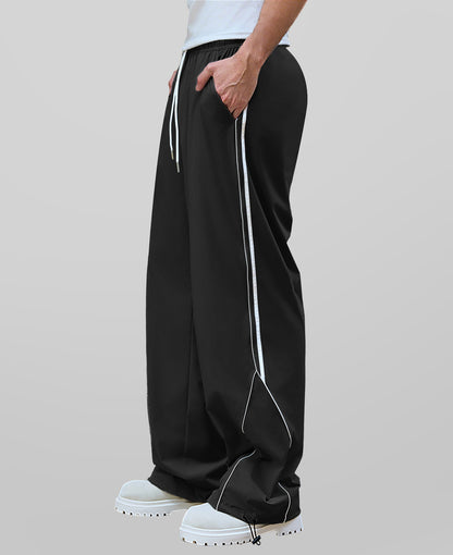 Man in black baggy wide leg sweatpants, side view, showing stripe detail and loose fit. White sneakers.