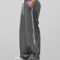 Man in dark grey baggy wide leg sweatpants, side view, showing stripe detail and loose fit. White sneakers.