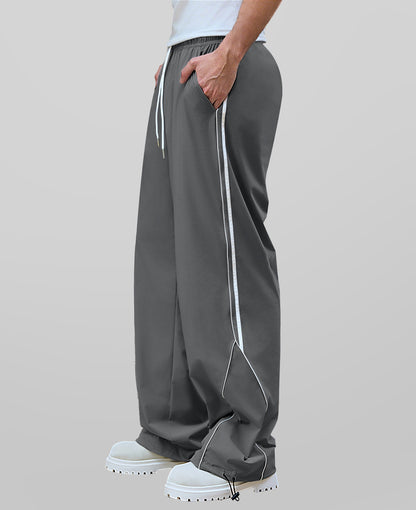 Man in dark grey baggy wide leg sweatpants, side view, showing stripe detail and loose fit. White sneakers.