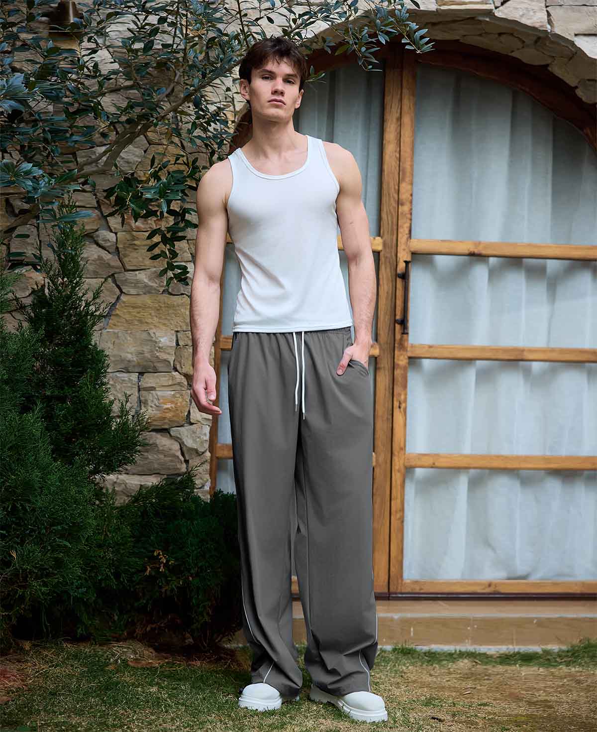 Full view of man wearing dark grey baggy wide leg sweatpants, white sneakers, front stance, showing overall look.