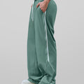 Man in green baggy wide leg sweatpants, side view, showing stripe detail and loose fit. White sneakers.