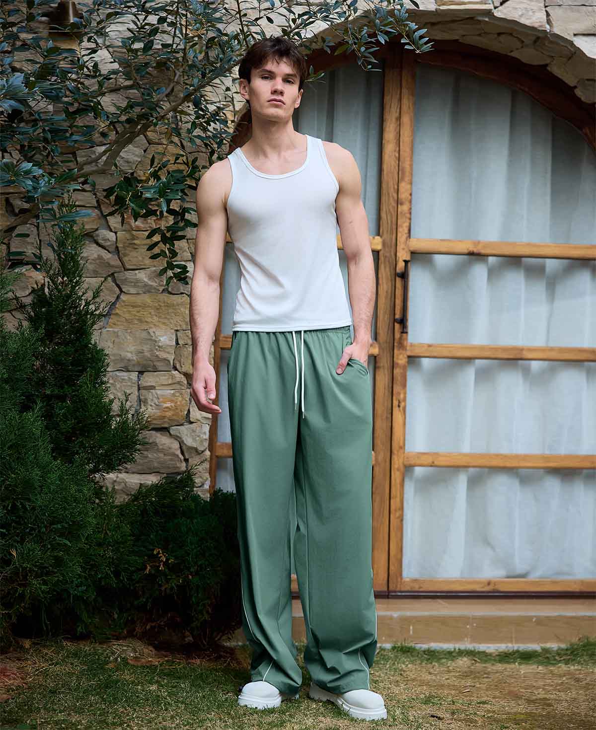 Full view of man wearing green baggy wide leg sweatpants, white sneakers, front stance, showing overall look.