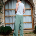 Man in green baggy wide leg sweatpants, white thick-soled shoes, back to camera, side stance on grass, showing loose fit and stripes.