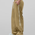 Man in khaki baggy wide leg sweatpants, side view, showing stripe detail and loose fit. White sneakers.