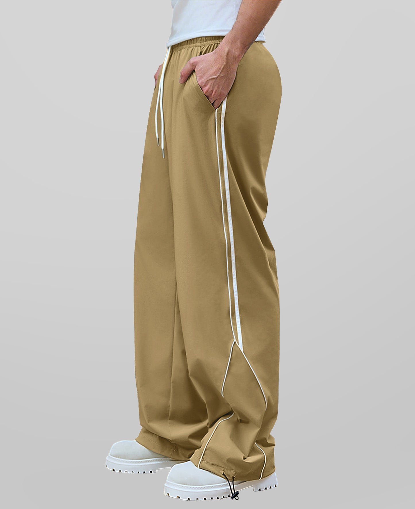 Man in khaki baggy wide leg sweatpants, side view, showing stripe detail and loose fit. White sneakers.
