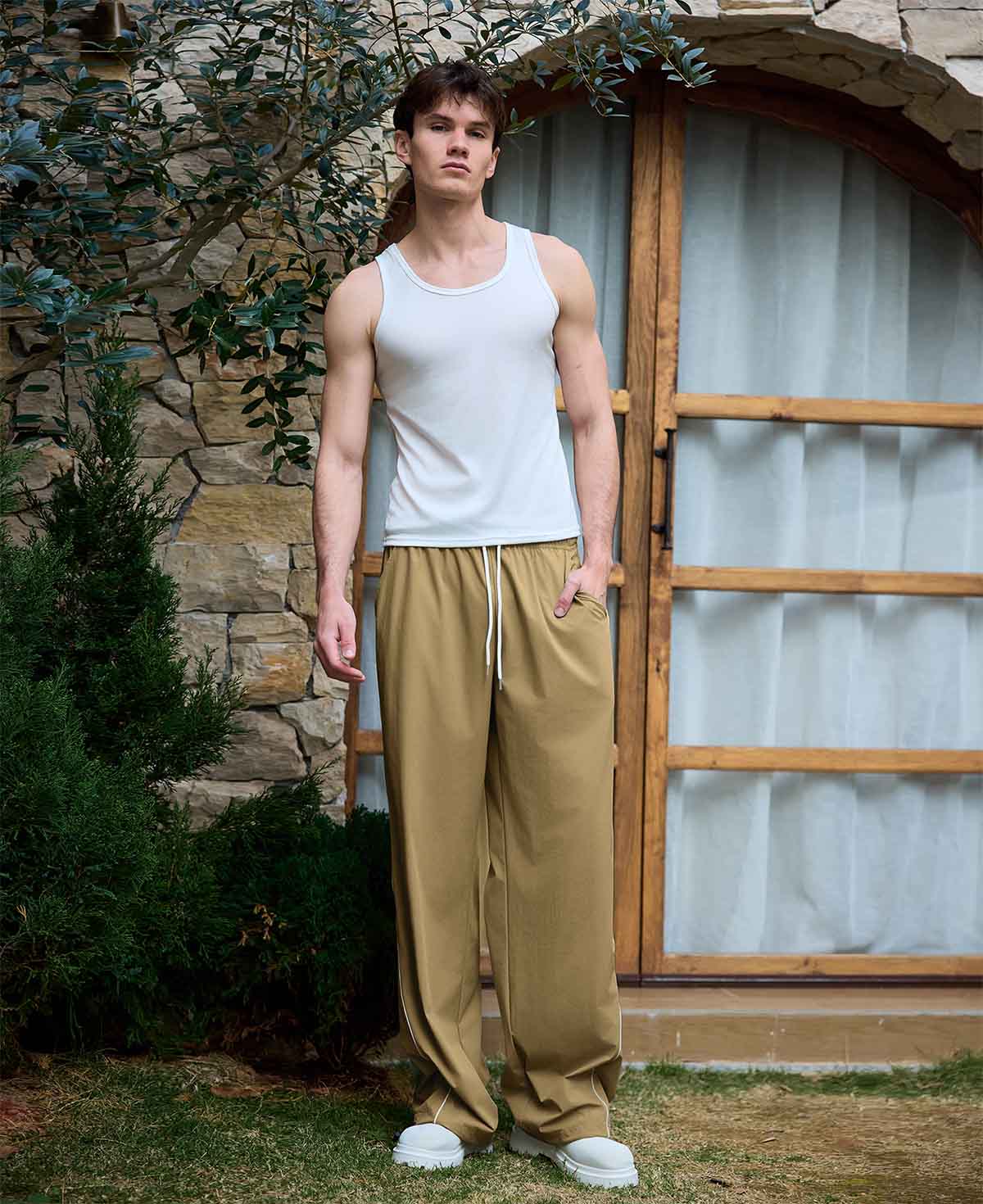 Full view of man wearing khaki baggy wide leg sweatpants, white sneakers, front stance, showing overall look.
