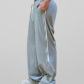 Man in lake blue baggy wide leg sweatpants, side view, showing stripe detail and loose fit. White sneakers.