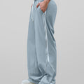 Man in light grey baggy wide leg sweatpants, side view, showing stripe detail and loose fit. White sneakers.