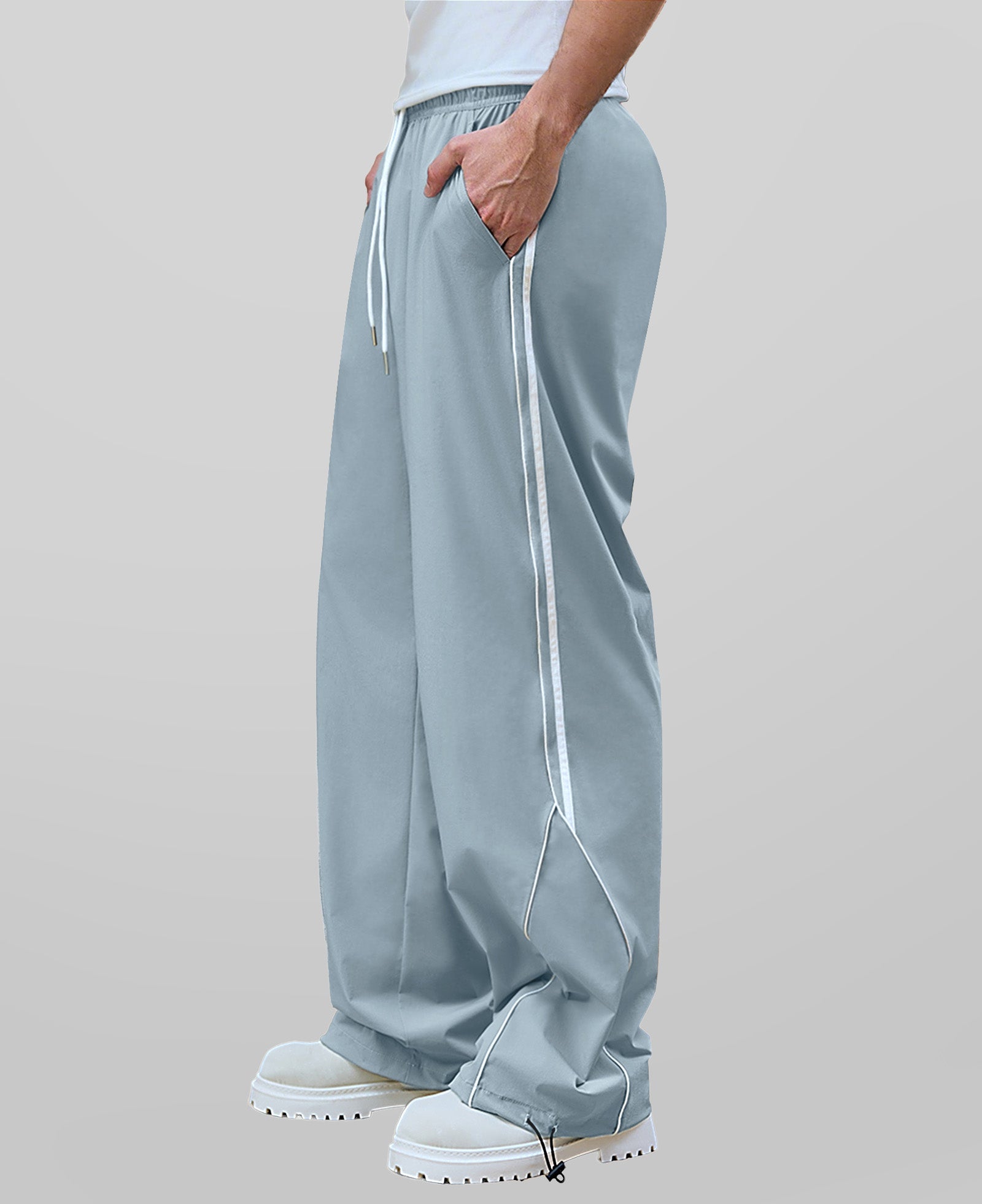 Man in light grey baggy wide leg sweatpants, side view, showing stripe detail and loose fit. White sneakers.